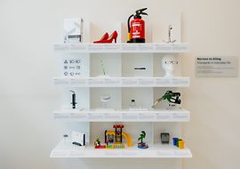 Abbildung des Exponats Normenregal aus der Ausstellung im NormenWerk bei DIN. 12 Normen aus dem Alltag sind hier abgebildet.